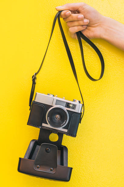 istock Hand holding a Vintage camera isolated at yellow wall 968935332