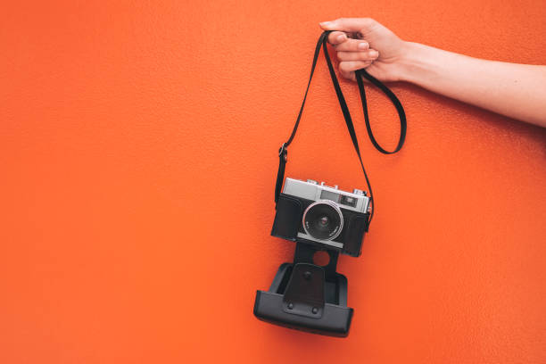 istock Hand holding a Vintage camera isolated at orange wall 968935350