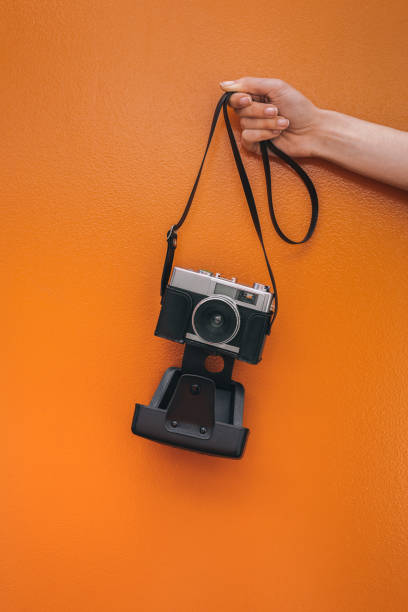 istock Hand holding a Vintage camera isolated at orange wall 968935356
