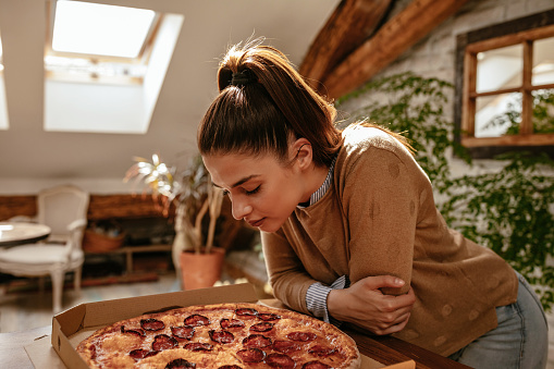 Cropped shot of an attractive young brunette eating pizza at home