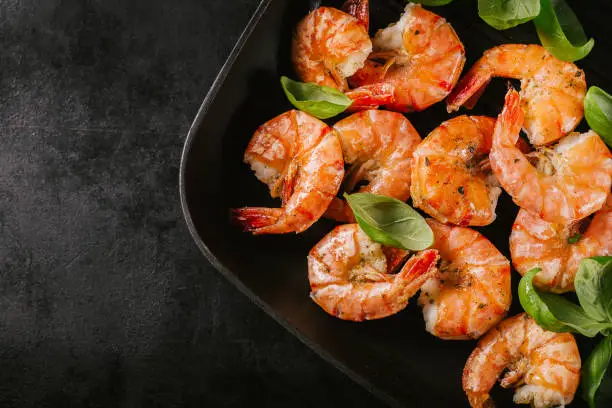 Fried grilled prawns with fresh herbs and basil on grill pan on dark background. Top view with place for text