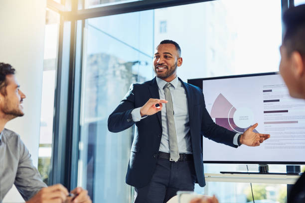 The goal was to grow and we did it Shot of a young businessman delivering a presentation to his colleagues in the boardroom of a modern office black business stock pictures, royalty-free photos & images