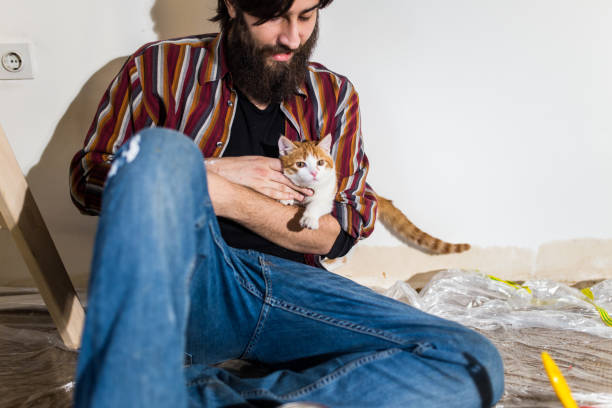 istock Hipster man with a beard painting a house and holding a kitty 968943782