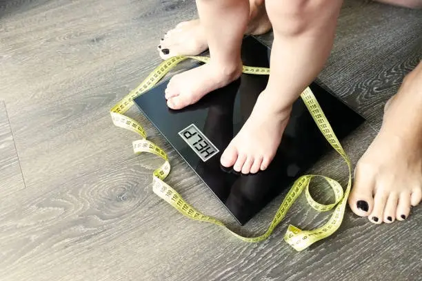 Photo of Help fat or obese child with toddler on weight scale, supervised by a parent