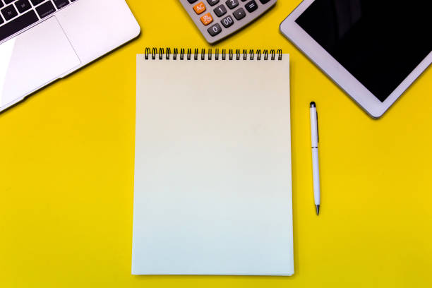 istock Yellow office desk table with  blank notebook, tablet, calculator and other office supplies. Top view with copy space. 968956824