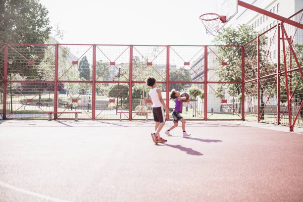 симпатичные смешанные расы братьев и сестер играть в баскетбол на открытом воздухе на баскетбольной площадке - basketball playing ball african descent стоковые фото и изображения
