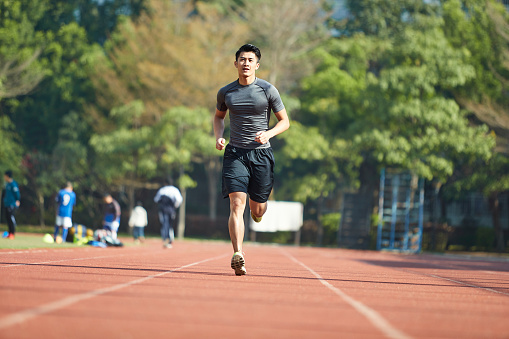 joven atleta asiático entrenamiento en pista de atletismo photo