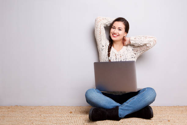 istock smiling young woman sitting on floor with laptop 968972652