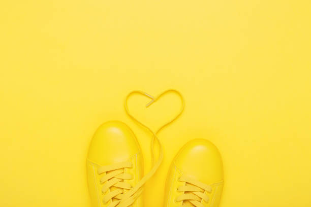 Pair of yellow shoes on yellow background. Pair of yellow shoes with heart made of shoelaces on yellow background. Trendy summer color, monochrome image. yellow shoes stock pictures, royalty-free photos & images