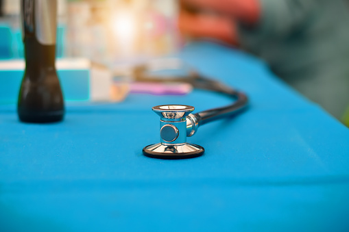 The stethoscope is placed on a blue table and there is a doctor in the back.