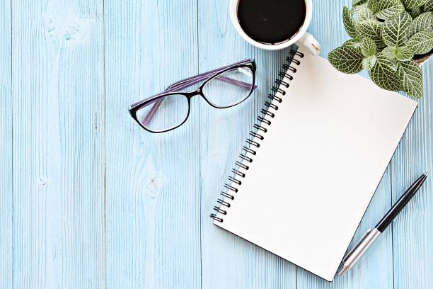 istock Open notebook with blank pages, coffee cup and eyeglasses on wooden desk table, top view or flat lay with copy space ready for adding or mock up 968979478