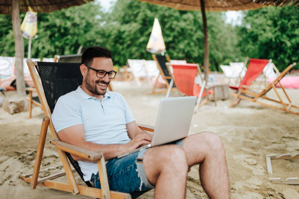 istock Young smiling man using laptop at the beach. 969013448