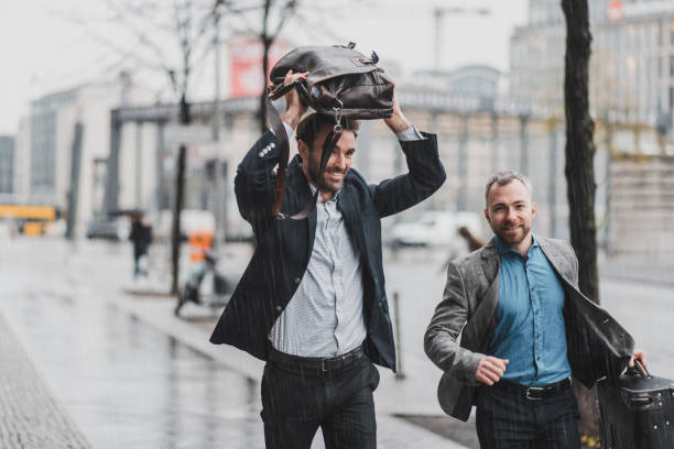 homme d’affaires en cours d’exécution sous la pluie, tenant une valise et une mallette - courir sous la pluie photos et images de collection