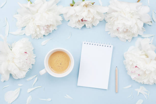 istock Morning coffee cup for breakfast, empty notebook and white peony flowers on blue pastel table top view. Woman working desk. Flat lay. 969035508