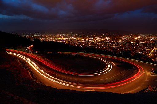 Breathtaking view of light streaks over road and night cityscape of Skopje in distance. Macedonia.