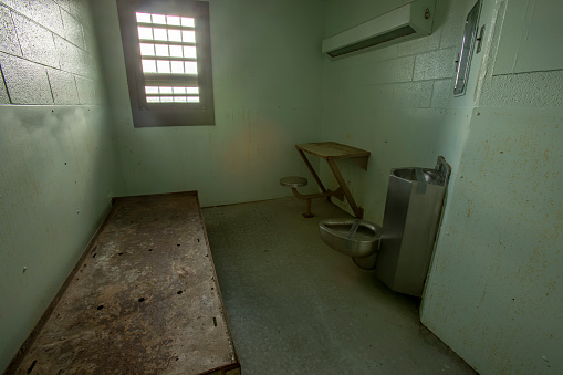 Interior of solitary confinement cell with metal bed, desk and toilet in old prison.