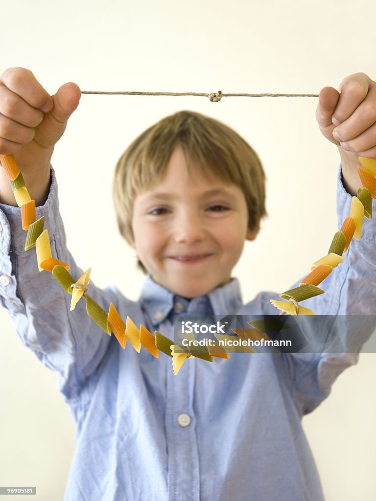 Young boy in blue shirt holding up a pasta necklace Happy little boy holding a homemade necklace made by himself out of dry pasta. Shallow depth of field with focus on the necklace. Pasta Stock Photo