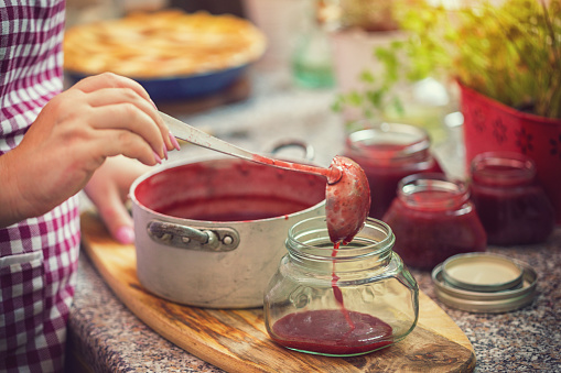 Young women preparing and canning fresh homemade strawberry jam, she pouring him into a jar