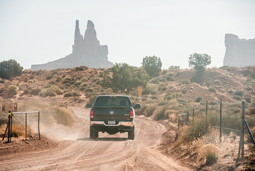 In Monument Valley, United States a large pickup truck drives along a dusty, dirt road leading towards rock formations in the background.
