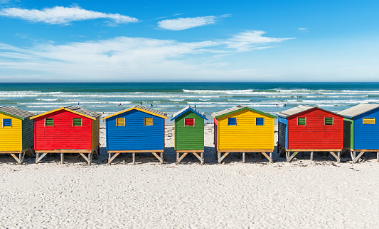 Symmetric landscape of Muizenberg beach with its famous colorful beach huts and surfers paradise near Cape Town, South Africa.