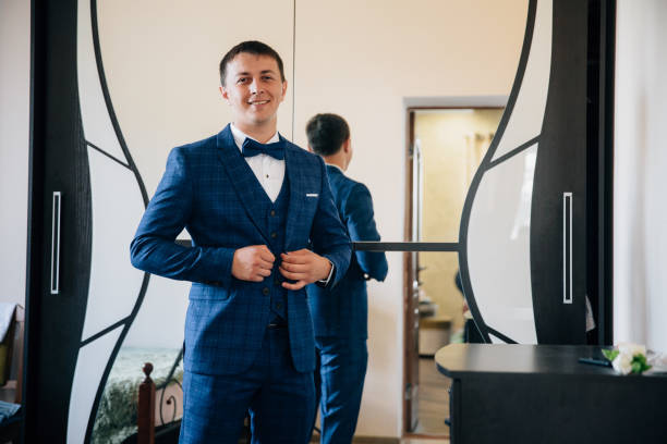 un homme d’affaires s’attache à sa veste. le gars mettre sur un beau costume, il se tient debout dans sa chambre avec un grand miroir et sourires - chain smoking photos et images de collection