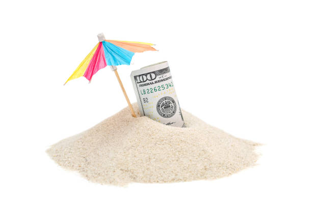 Rolled up money with beach umbrella on the heap of sand. Isolated on white. stock photo