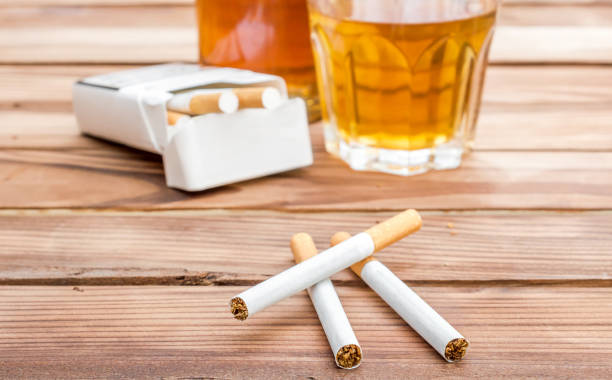 Cigarettes with alcohol drinks on wooden table. Social issues. stock photo