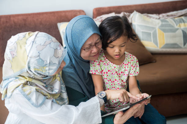 trois générations de femmes qui cherchent à une tablette - grandparent senior adult child reading photos et images de collection