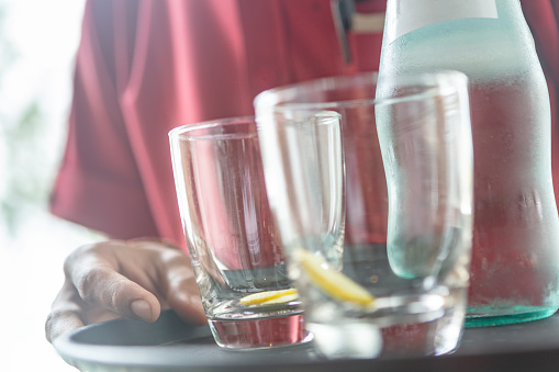 Wait staff serving water, carrying water bottle and drinking glasses on serving tray