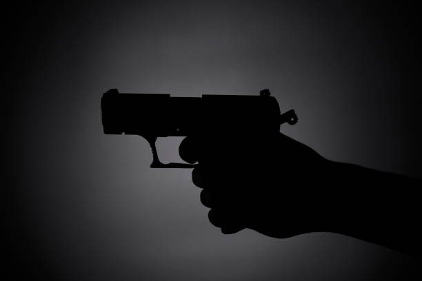 black silhouette of a male aiming with a gun in the dark