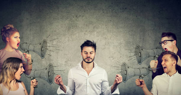 meditating businessman paying no attention to crowd of screaming angry people Impassive meditating young businessman paying no attention to crowd of screaming in megaphone angry people ignoring stock pictures, royalty-free photos & images