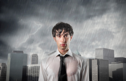Man in wet shirt in front of city buildings being rained on
