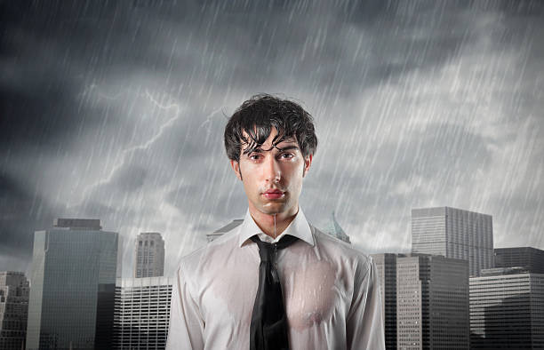 Man in wet shirt in front of city buildings being rained on stock photo
