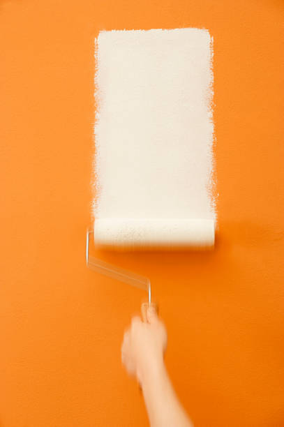 istock PAINT ROLLER APPLYING WHITE PAINT TO ORANGE WALL 969153294