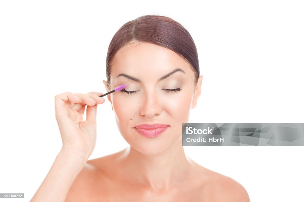 Woman applying eyelash serum essential oil on eyelashes with makeup mascara brush Woman applying eyelash serum essential oil on eyelashes with makeup mascara brush. Closeup portrait photo of appealing brunette girl with eyes closed on white background, mixed race model Eyelash Stock Photo