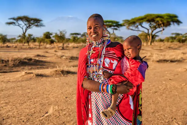 African mother from Maasai tribe carrying her baby , Kenya, Africa - Mount Kilimanjaro on the background. Maasai tribe inhabiting southern Kenya and northern Tanzania, and they are related to the Samburu.