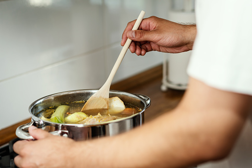 man mixes the delicious and fragrant broth in a pot on the gas stove in the kitchen