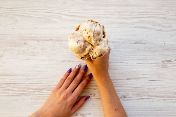 Woman's hands holding caramel ice cream on white wooden background, top view. From above.