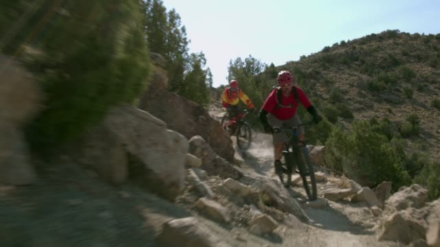 Two Men Ride Mountain Bikes Down Rocks in the Desert