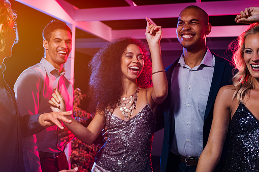 Cheerful girl dancing at night party with her friends. Beautiful young woman and smiling men having fun at nightclub. Group of multiethnic young people at club having fun at new year's eve.
