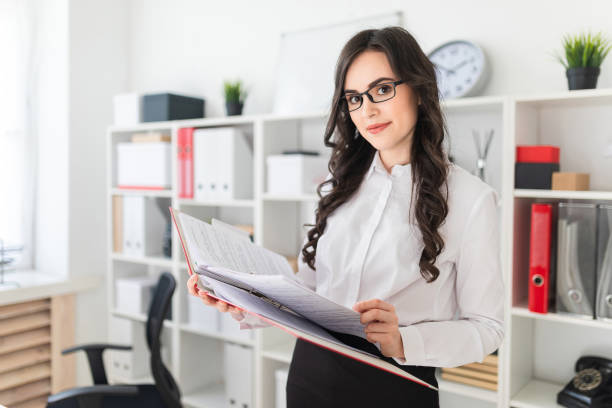 istock Beautiful young girl stands in the office thumbs a folder with documents. 969259464