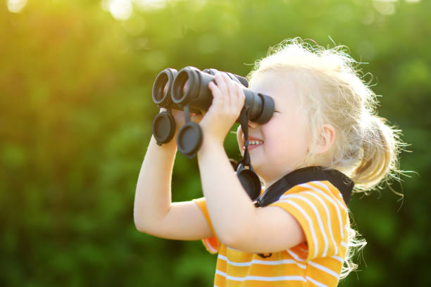 istock Funny little girl looking through binoculars on sunny summer day 969262644