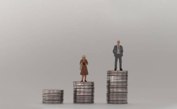 A miniature man and a miniature woman standing on a stack of coins of different heights. The concept of a gender pay gap. stock photo