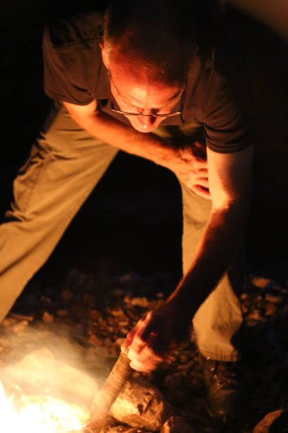 istock Man Tending Stoking Camping Campfire with Stick 969297192