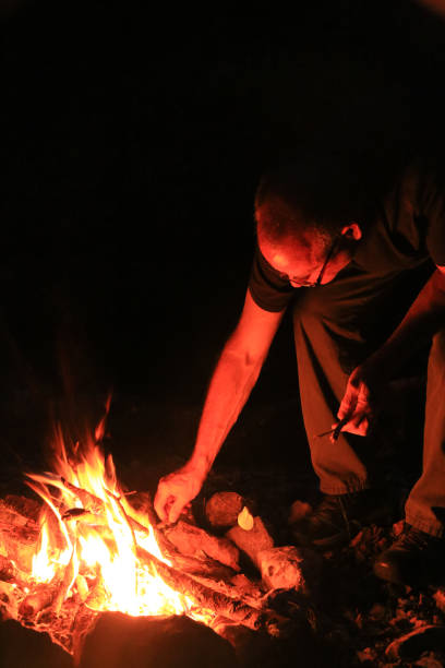 istock Man Tending Stoking Camping Campfire with Stick 969297908