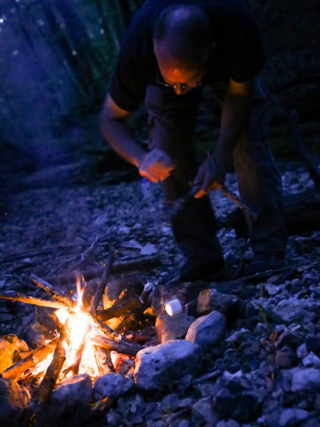 Man Tending Camping Campfire at Twilight, Dusk