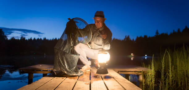 A man shows a fish caught in the light of a lamp. Evening twilight. tinca tinca stock pictures, royalty-free photos & images
