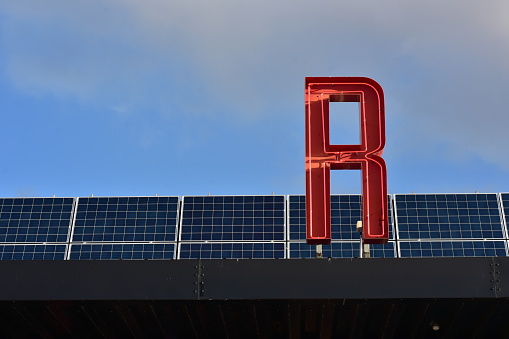 Red fluorescent tube sign letter on roof covered with solar panels.