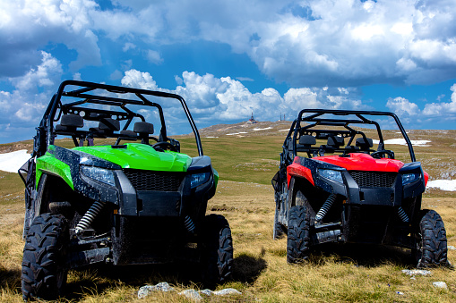 Parked ATV and UTV, buggies on mountain peak with clouds and blue sky in background.