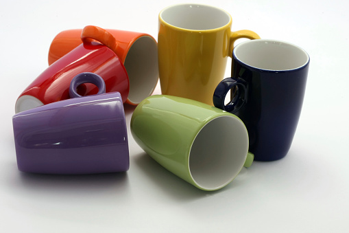 Stock photo of close-up view of retail display shelves containing rows of pottery mugs and cups in rainbow colours in shades of red, orange, yellow, blue and green glazes, glazed and fired in kiln.